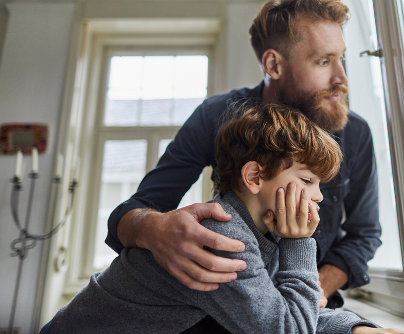 Vader slaat zijn arm om zijn zoon heen, ze kijken samen naar buiten