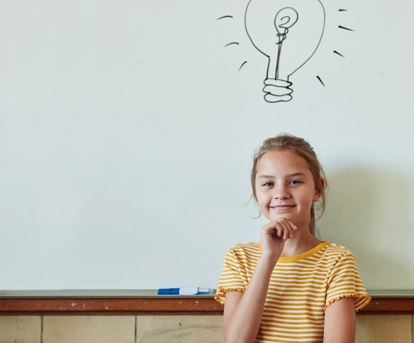 meisje staat voor een schoolbord waarop een gloeilamp is getekend